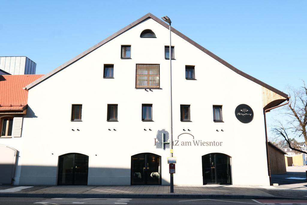 Franz am Wiesntor in Rosenheim mit weißer Fassade, braunem Dachrand und mehrfachen rechteckigen Fenstern; Logo und Straßenszene im Vordergrund