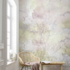 Pastellfarbene Wandtapete mit zarten Blumenmotiven in Rosa, Gelb und Lila aus der Elysian Kollektion von k’moor, abgebildet in einem hellen Raum mit Rattan-Stuhl