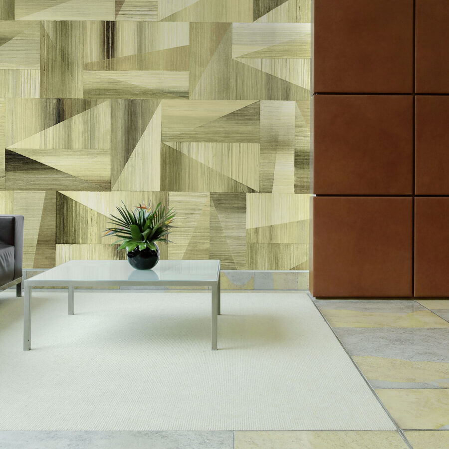 Geometrische Holzoptik Wandgestaltung: Wand mit musternden Holzpaneelen in warmen Braun-Tönen, links eine graue Ledercouch, mittig glasiger Couchtisch mit Pflanze, rechte Wand mit braunen Quadraten