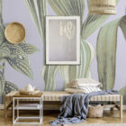 Botana de Sol Wanddesign zeigt eine lilafarbene Tapetenwand mit großem Blattmuster, ergänzt durch Holzmöbel, Körbe und dezentes Dekor in einem modernen Raum