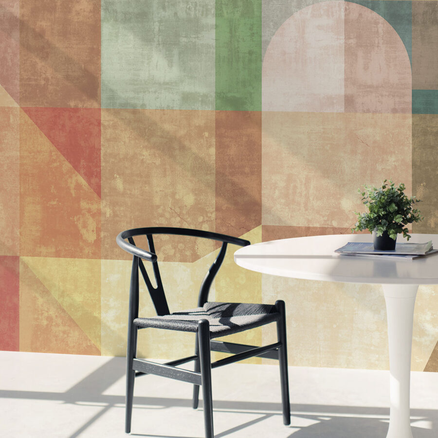 Solljus mehrfarbige geometrische Wandgestaltung als Tapetenmuster; dunkler Stuhl neben weißem Tisch, k‑moor Wanddesign