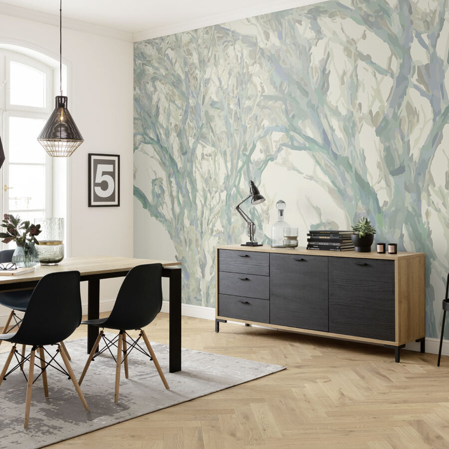Rustling Trees Wanddesign in hellem Esszimmer: blau-grüne Baumwandmalerei hinter einer Holzkonsole, daneben Esstisch mit schwarzen Stühlen und dekorativen Elementen