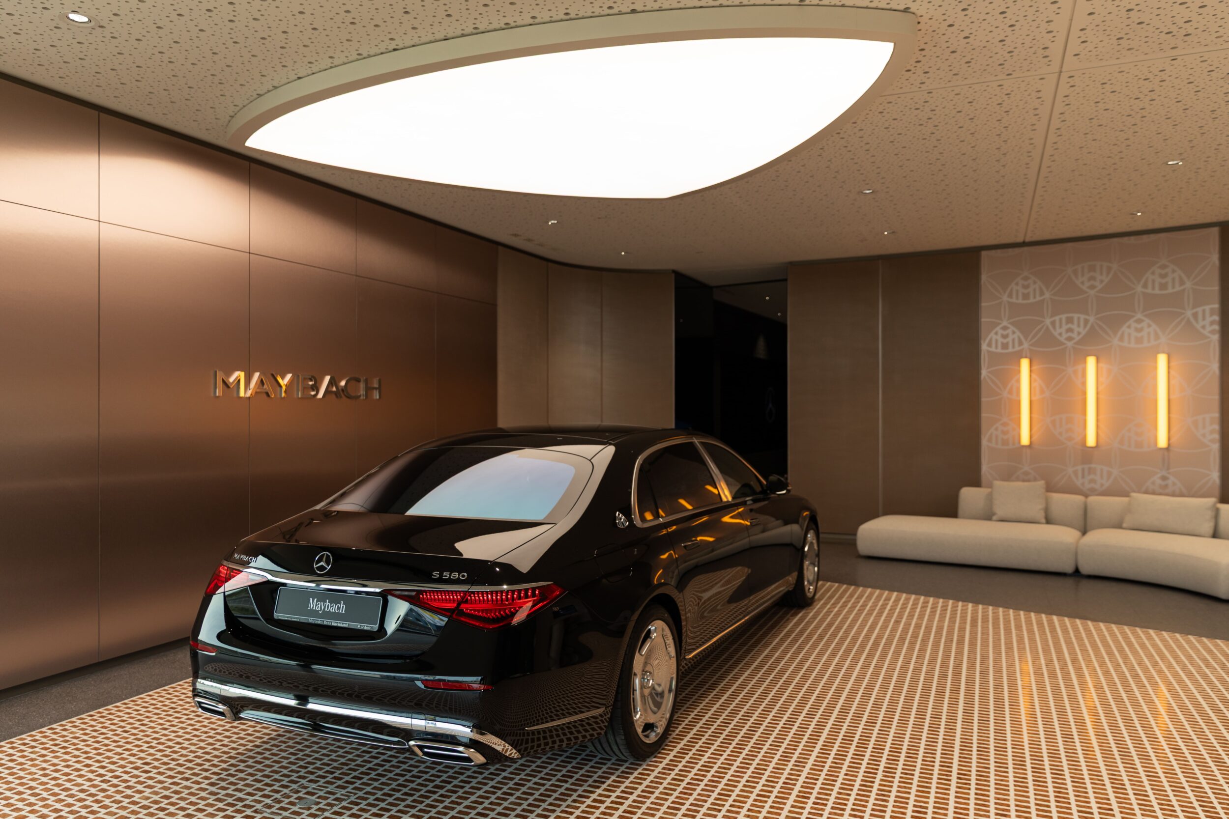 Schwarzer Maybach S680 steht glänzend vor einer modernen Lobby mit bronzefarbenen Wänden und weißem Sofa im Tev Store Köln Showroom
