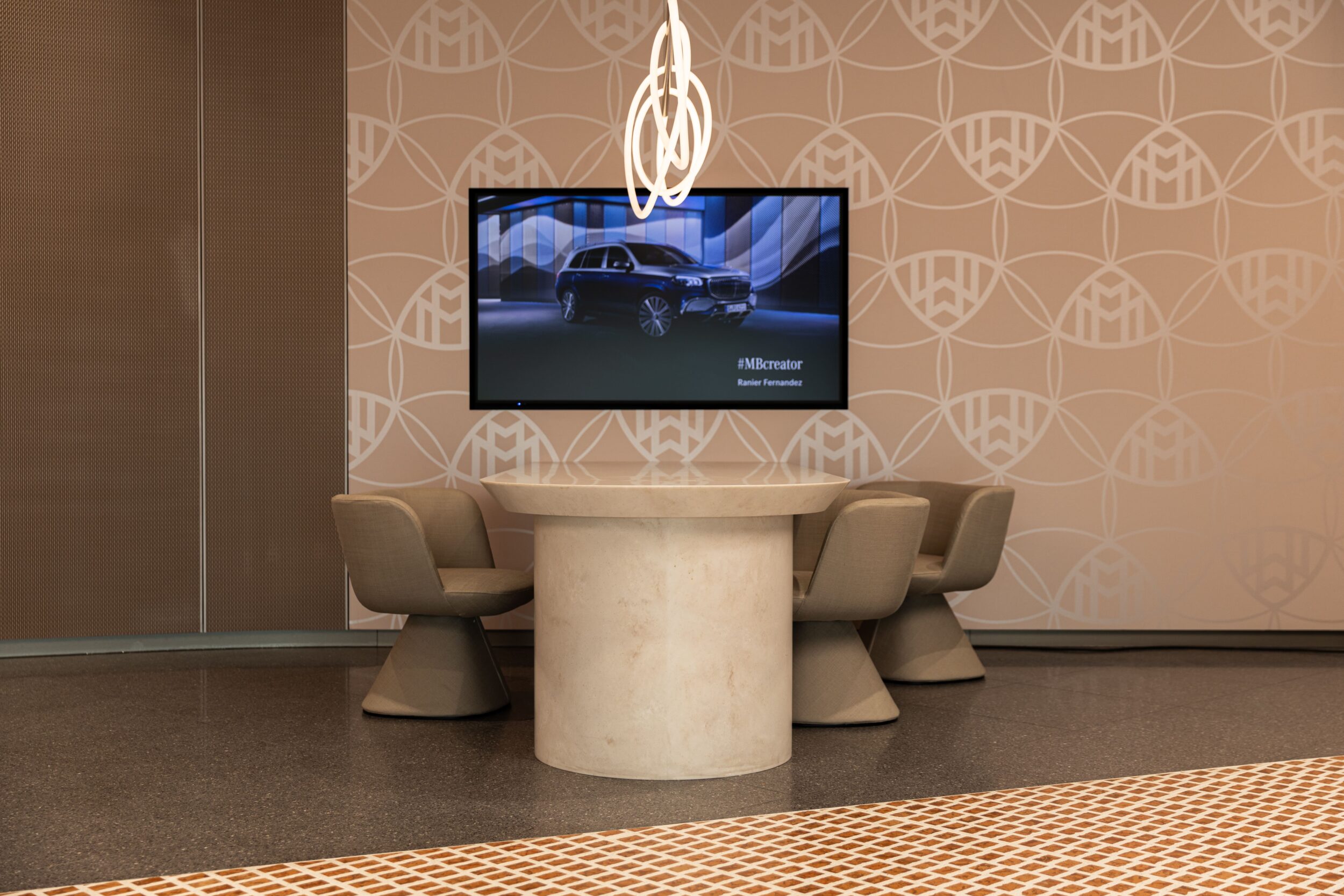 Tomislav Vukosav – Innenraum von tev_store_koeln mit beige Marmortisch, runden Bech chairs, wandseitigem Muster und einem Flachbildschirm