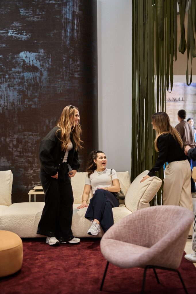 Auf dem Salone del Mobile sind Gespräche in einer Lounge mit dunkelgrauer Texturwand und grünen Vorhängen zu sehen, im Stil von k’moor.