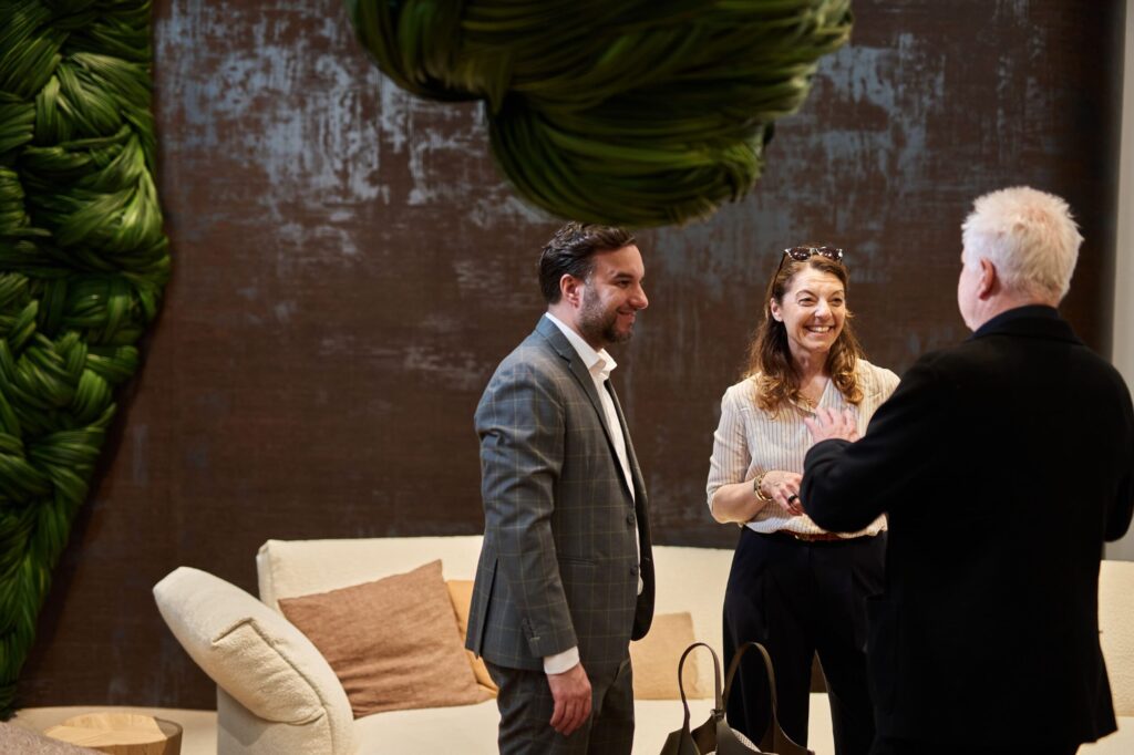 Beim Austausch im Messeumfeld stehen Besucher zusammen, während k’moor die Wandfläche für Walter Knoll beim Salone del Mobile gestaltet, mit brauner Wand und grüner Deko.