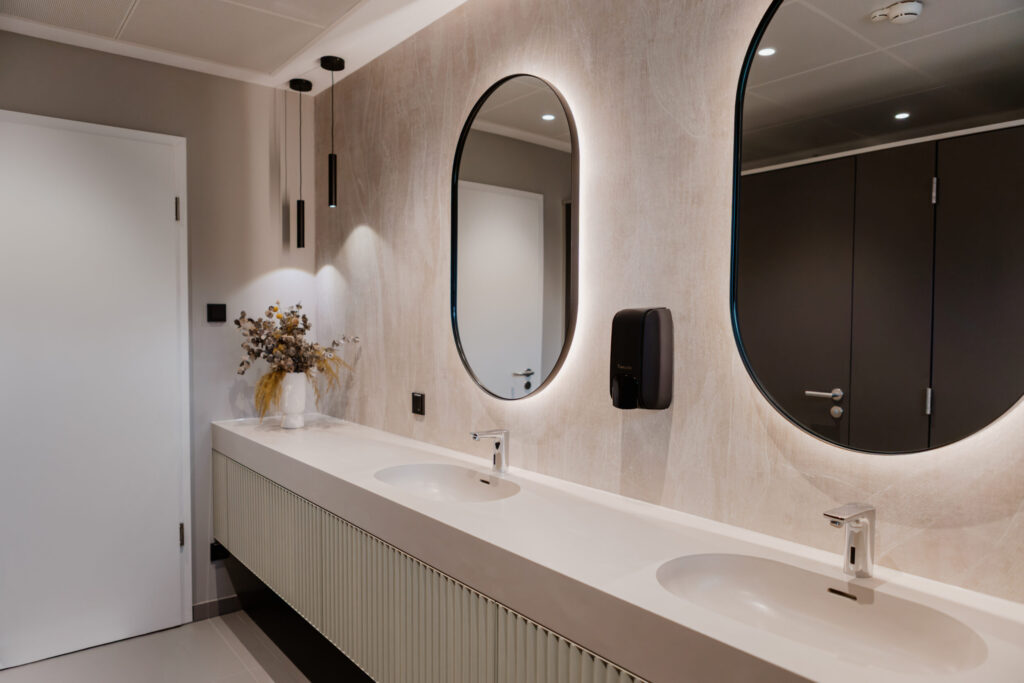 k-moor- Modern washroom vanity, Neugestaltung moderner Waschräume, k'moor wall design A modern washroom vanity with twin round mirrors, beige textured wall design, and a long white countertop with integrated basins.