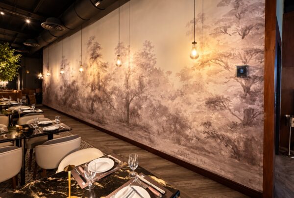 Gedeckte Tische und warm leuchtende Pendellampen vor dem sepiafarbenen Waldmotiv im Baires Grill in Miami.